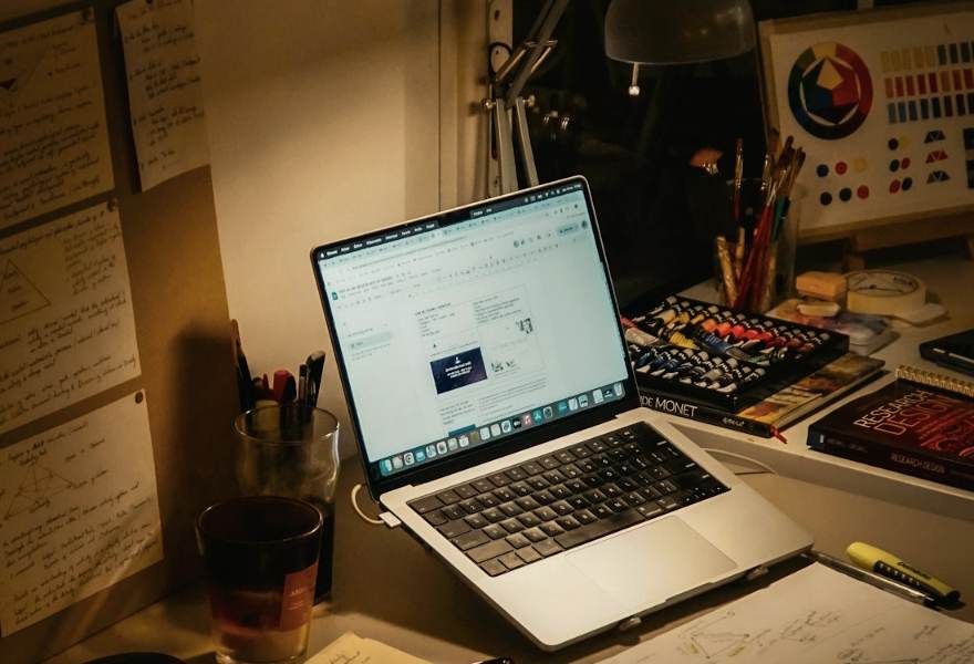 A desk at night with a laptop, notes and books